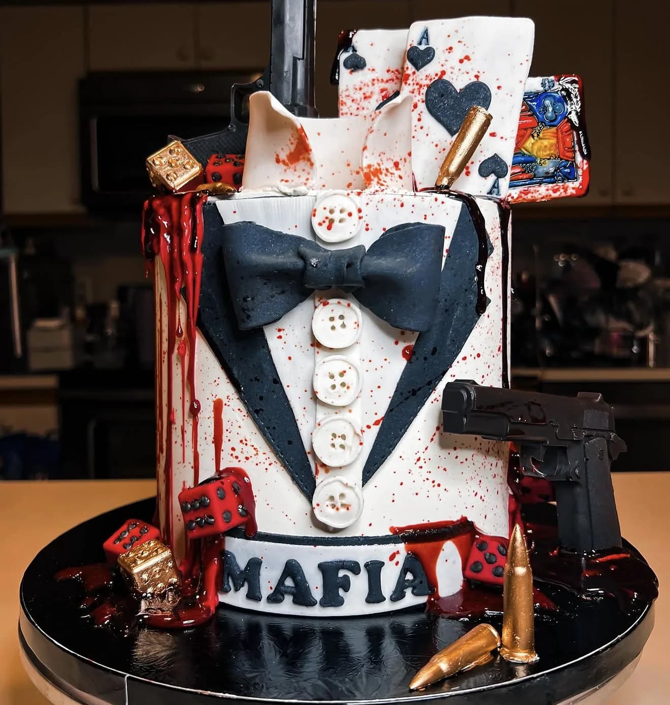 Mafia-themed cake with fondant tuxedo bowtie, blood splatter, playing cards, bullets and pistol
