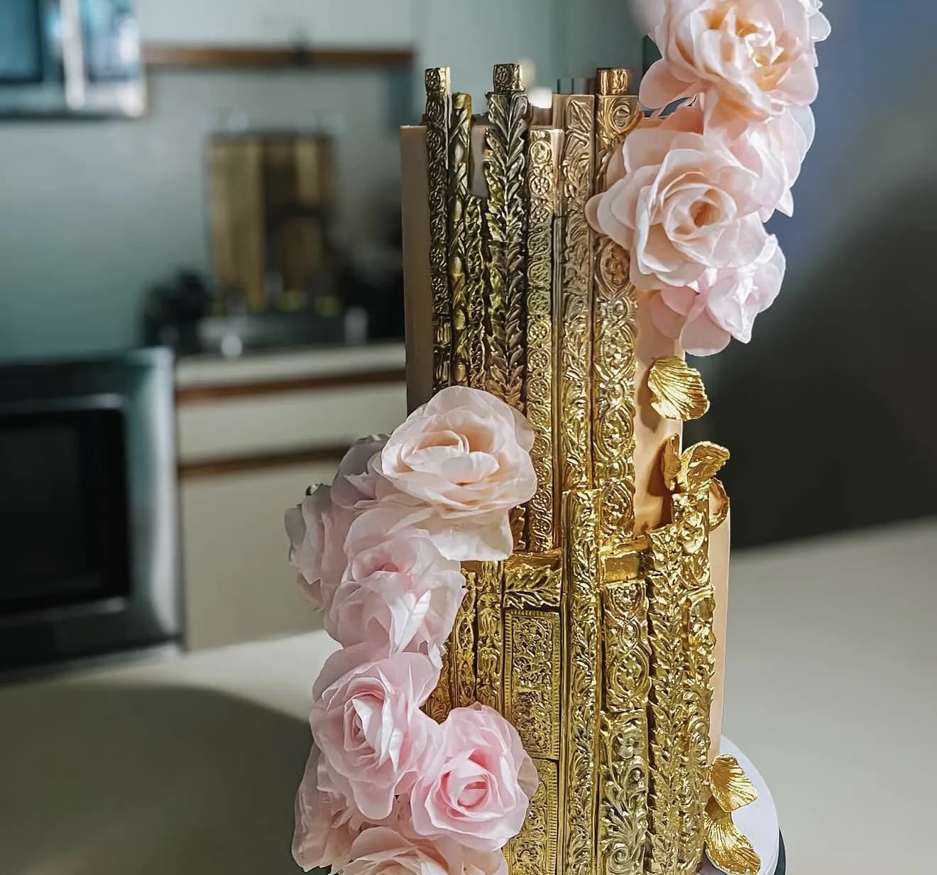 Tiered cake with ornate gold baroque panels, blush sugar roses and gilded ginkgo leaves