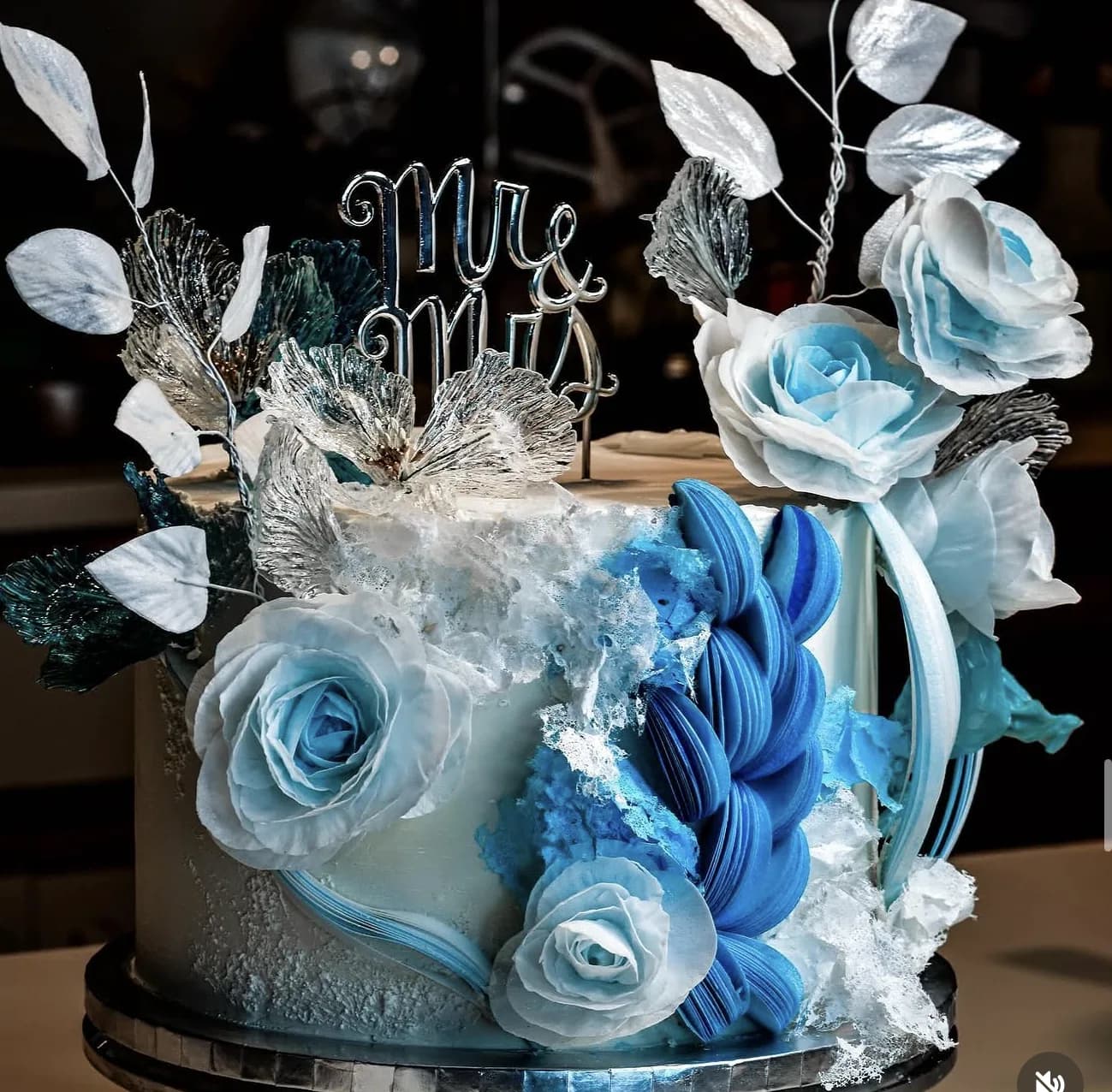White wedding cake with icy blue sugar rose petals, silver leaves and Mr and Mrs wire topper