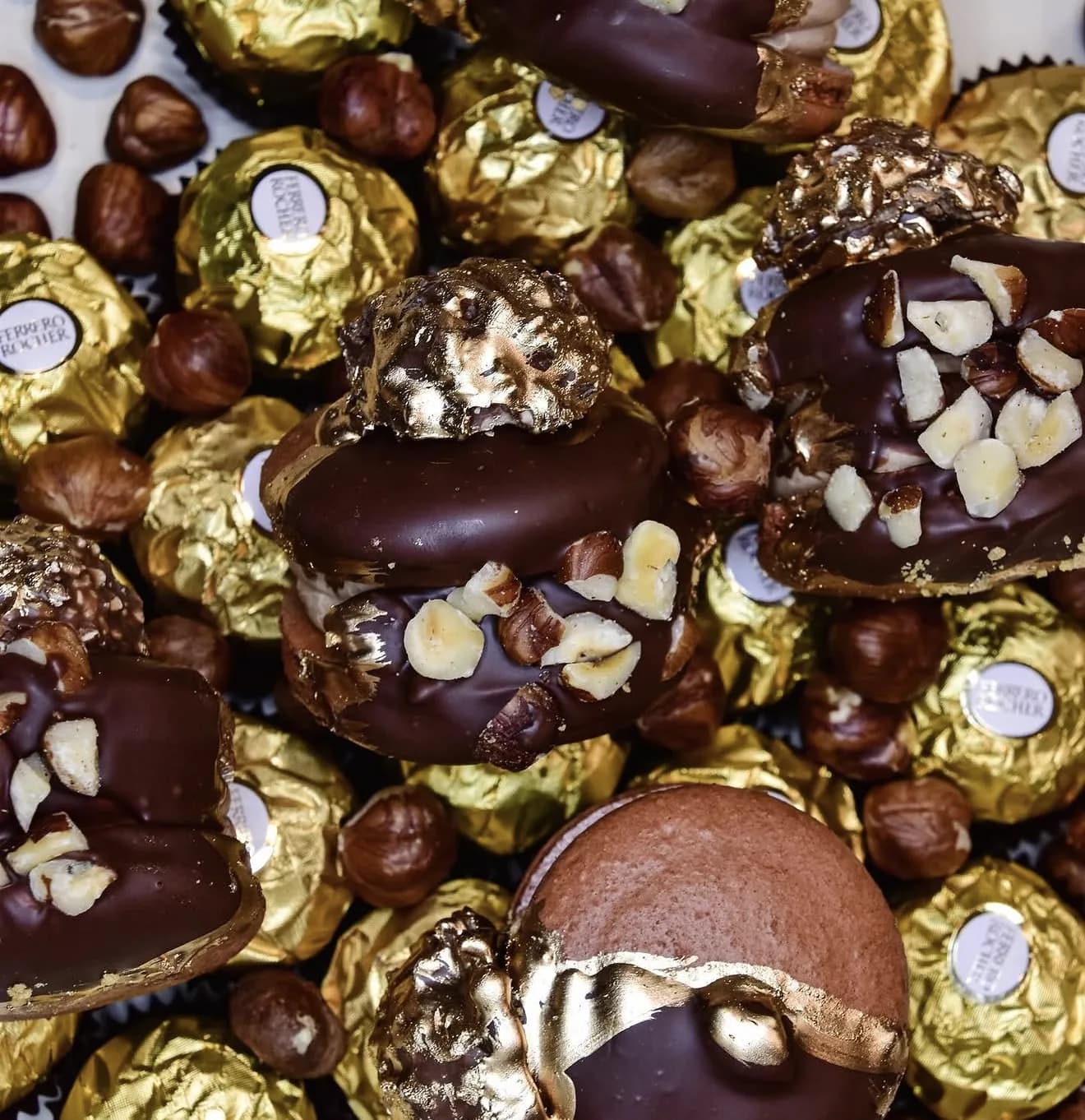 Pile of chocolate macarons and gold-foiled Ferrero candies with scattered hazelnuts