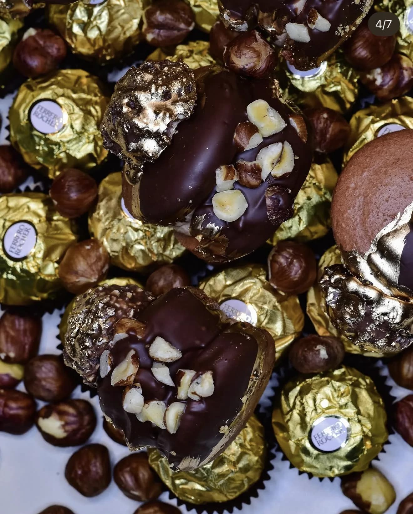 Heart-shaped chocolate macaron crowned with chopped hazelnuts nestled among Ferrero candies