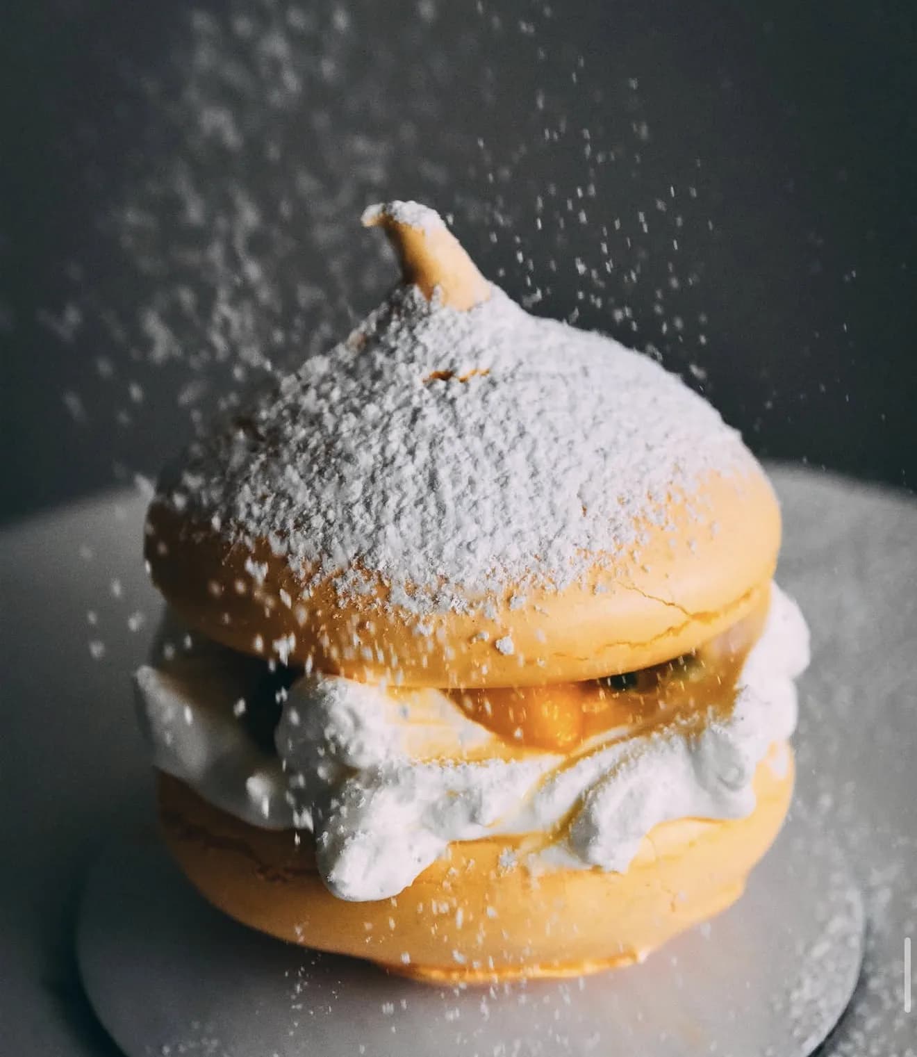 Yellow pavlova with powdered sugar falling mid-air over peaked meringue with cream filling