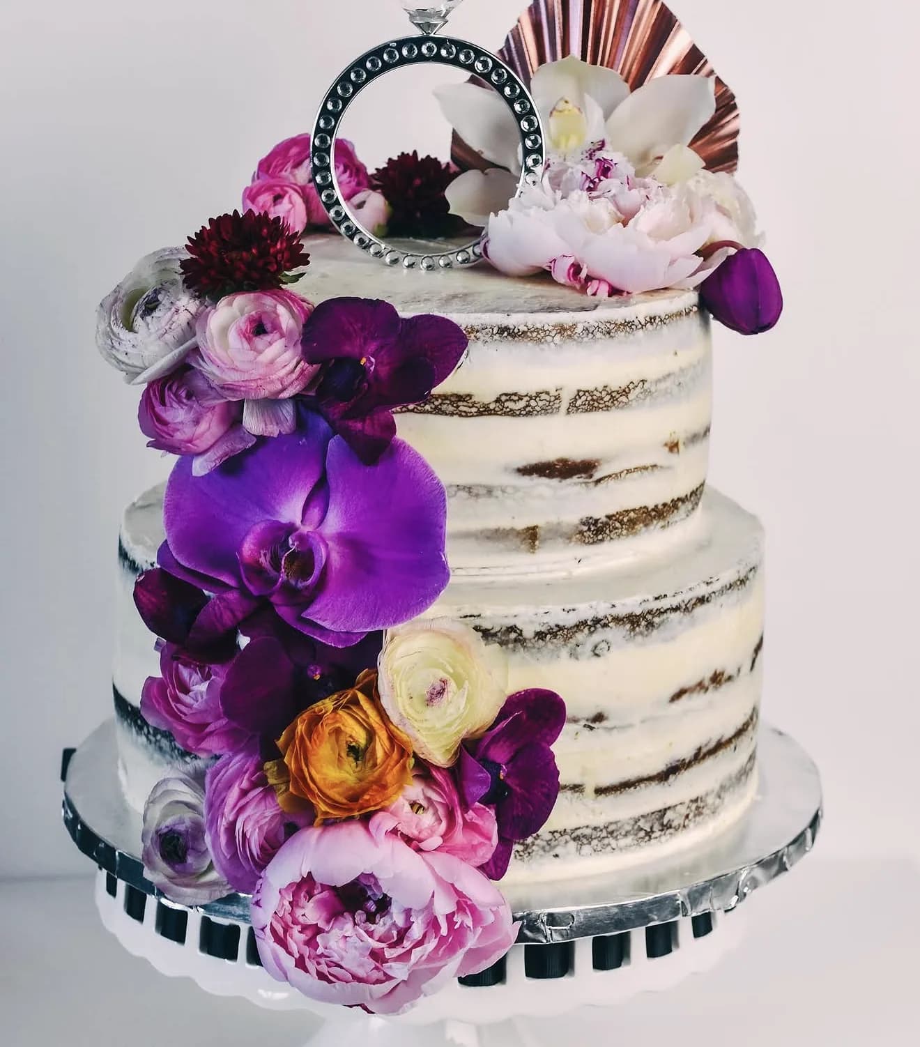Semi-naked cake with diamond ring topper cascading purple orchids pink peonies and ranunculus