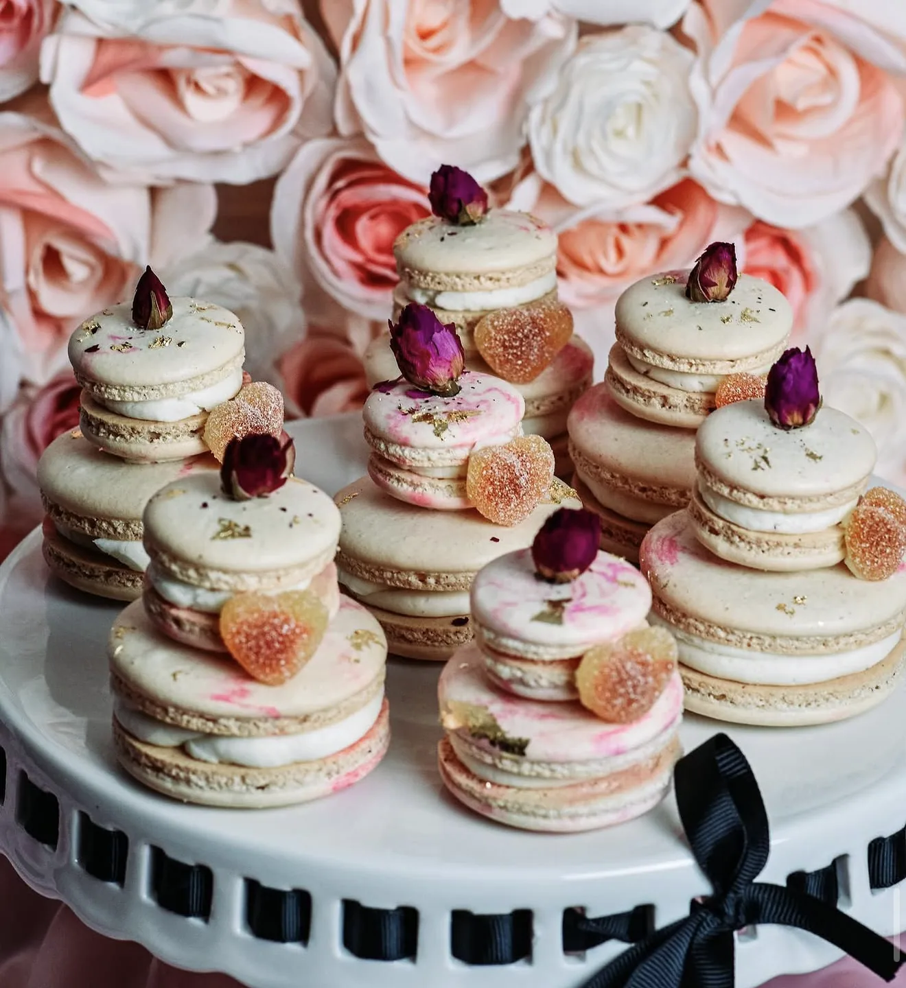 Close stack of cream-toned macarons with pink marbling gold leaf and dried rosebud tops