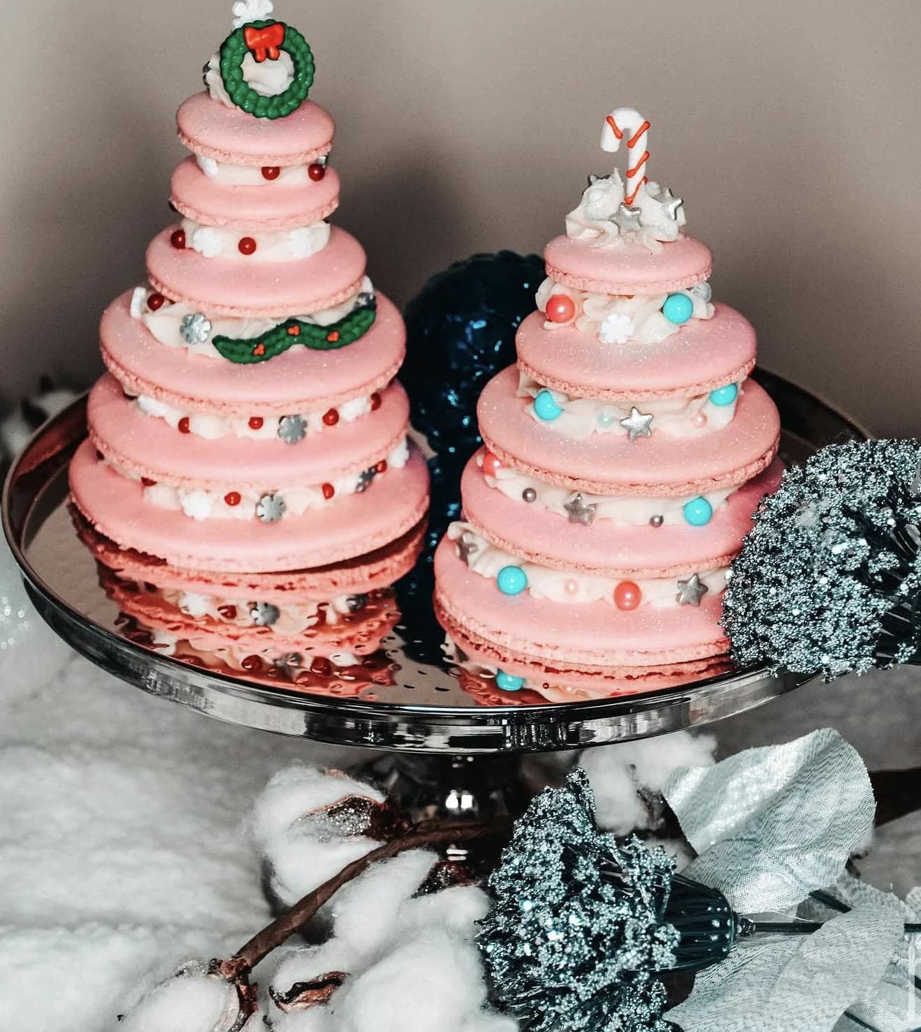 Teal and pink macaron Christmas tree towers on glass plate beside snow cotton and lights