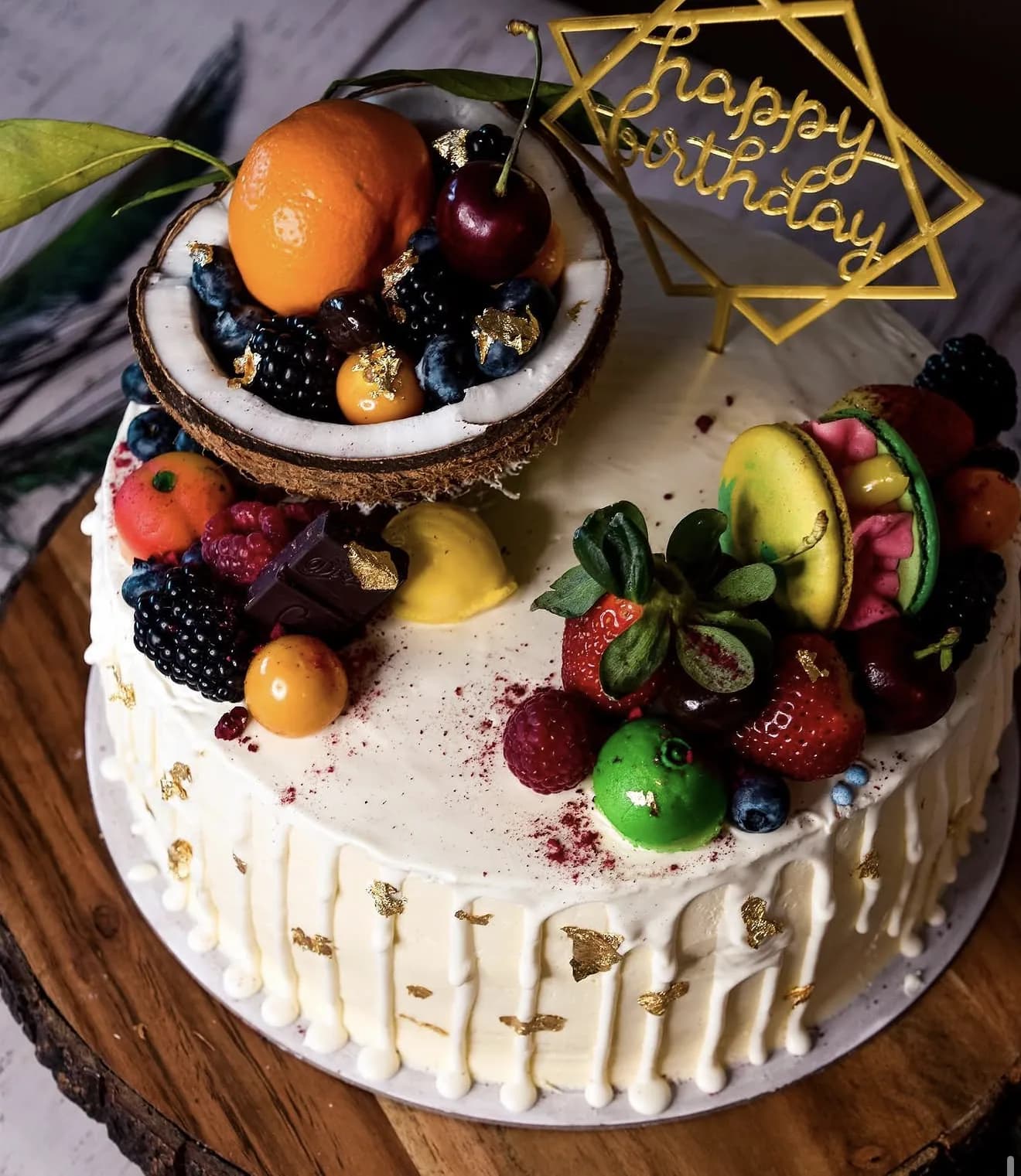 Side view white drip cake with fruit loaded coconut bowl on wood round rustic base