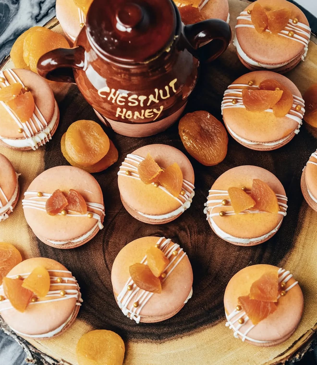 Apricot macarons with white drizzle apricot slices and sprigs of dried lavender on dark surface