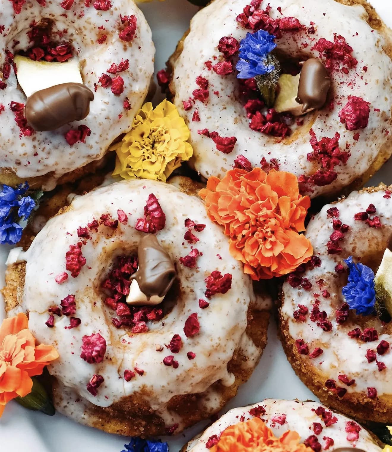 Overhead raspberry crumble donuts with chocolate caramel candies and marigold flower petals